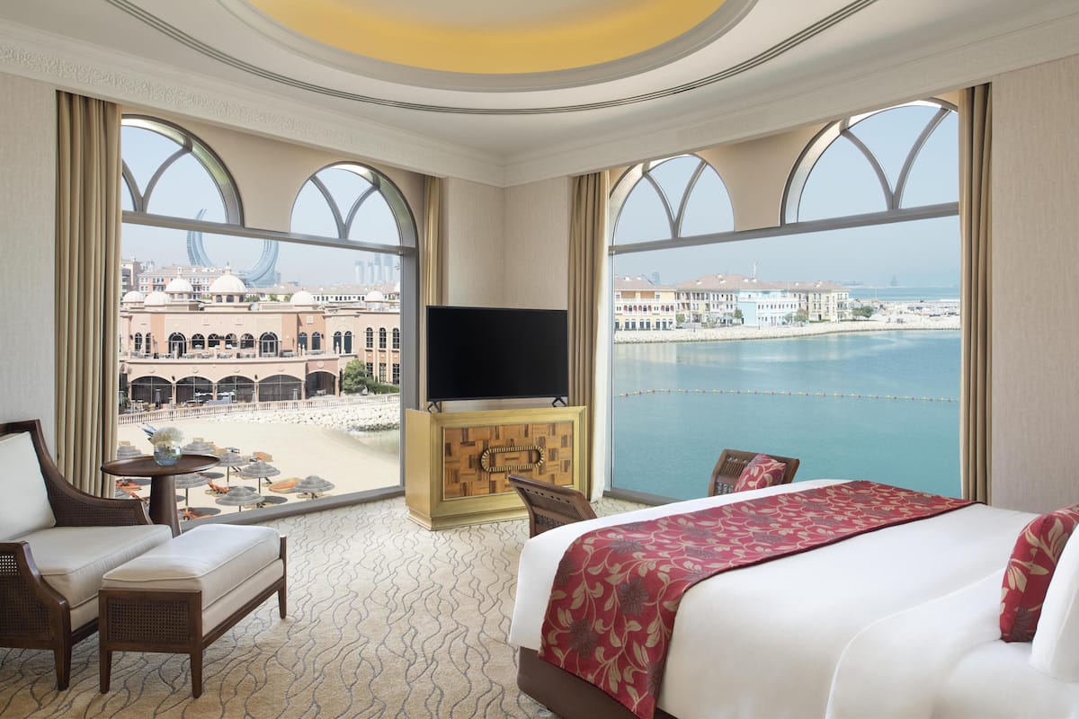 Une chambre d’hôtel dotée d’un grand lit, d’une télévision, d’un coin salon avec une table et de grandes fenêtres offrant une vue sur la plage et le paysage urbain.