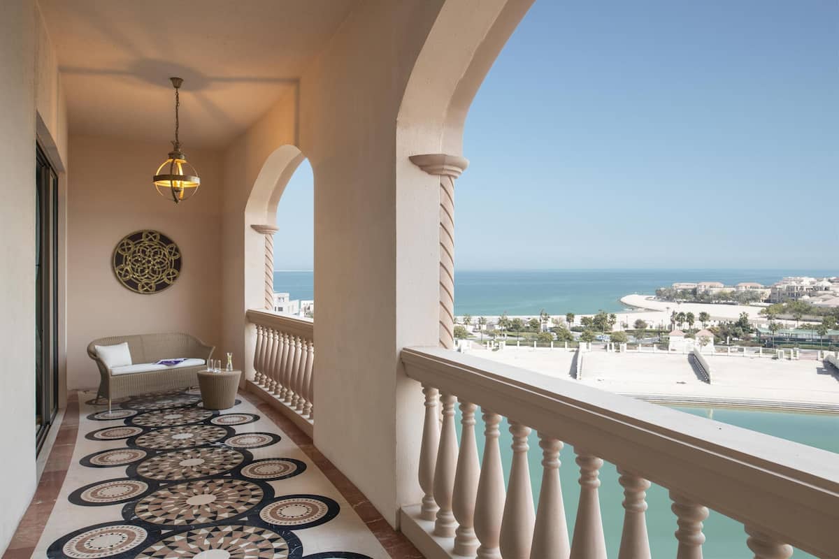 Un balcon doté d’un sol à motifs, d’un canapé en osier, d’un luminaire suspendu et offrant une vue sur la mer et la plage.