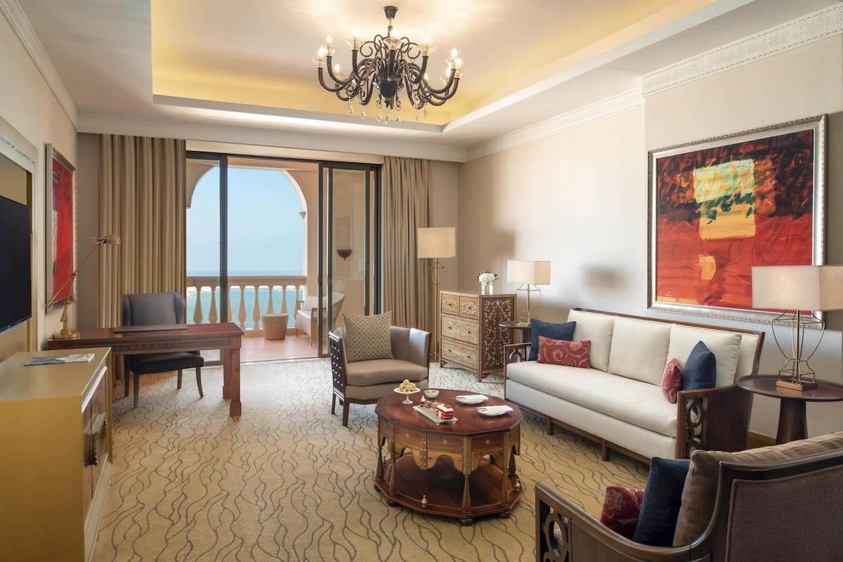 Une chambre d’hôtel spacieuse dotée d’un grand balcon, d’un canapé, d’une table à manger et d’un lustre.