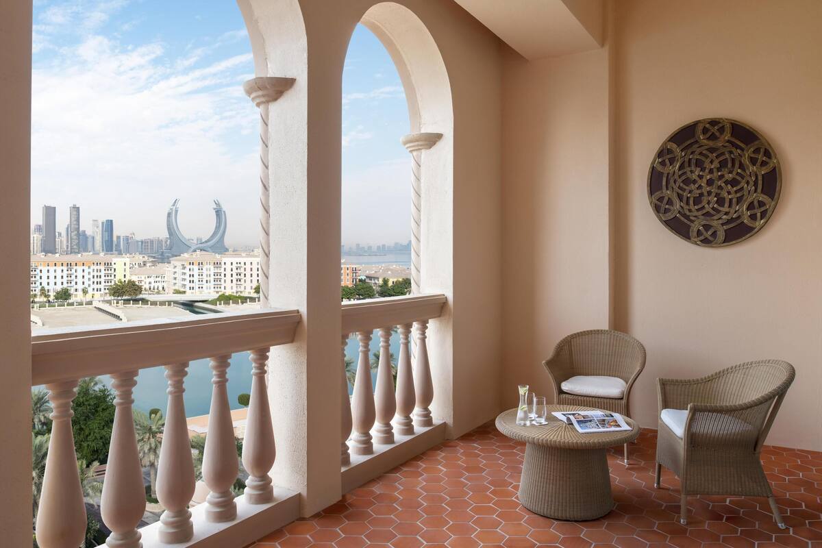 Un balcon offrant une vue sur le paysage urbain, avec une table ronde, deux chaises et un élément décoratif mural.