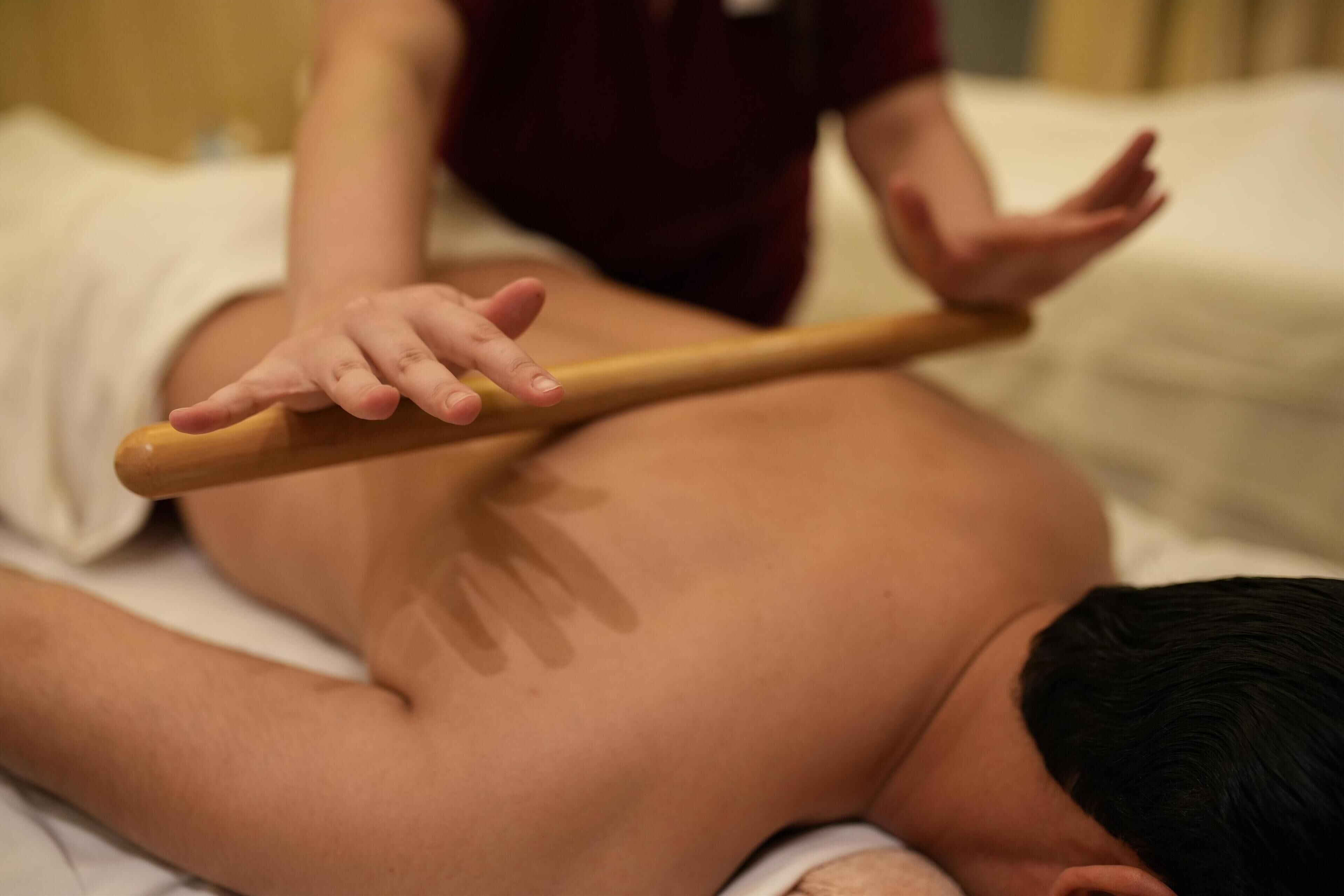 A person receiving a back massage with a wooden tool.