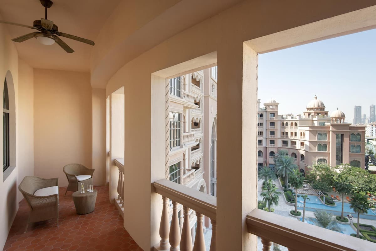Un balcon doté de meubles en osier, d’un ventilateur de plafond et offrant une vue sur un grand bâtiment orné de coupoles.