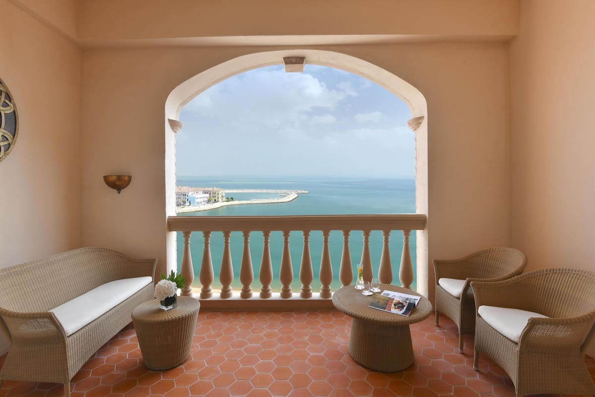 Un balcon doté de meubles en osier, offrant une vue sur la mer et agrémenté d’une balustrade blanche.