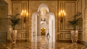 Un hall imponente con piso de mármol, apliques de pared ornamentados y grandes jarrones con plantas.