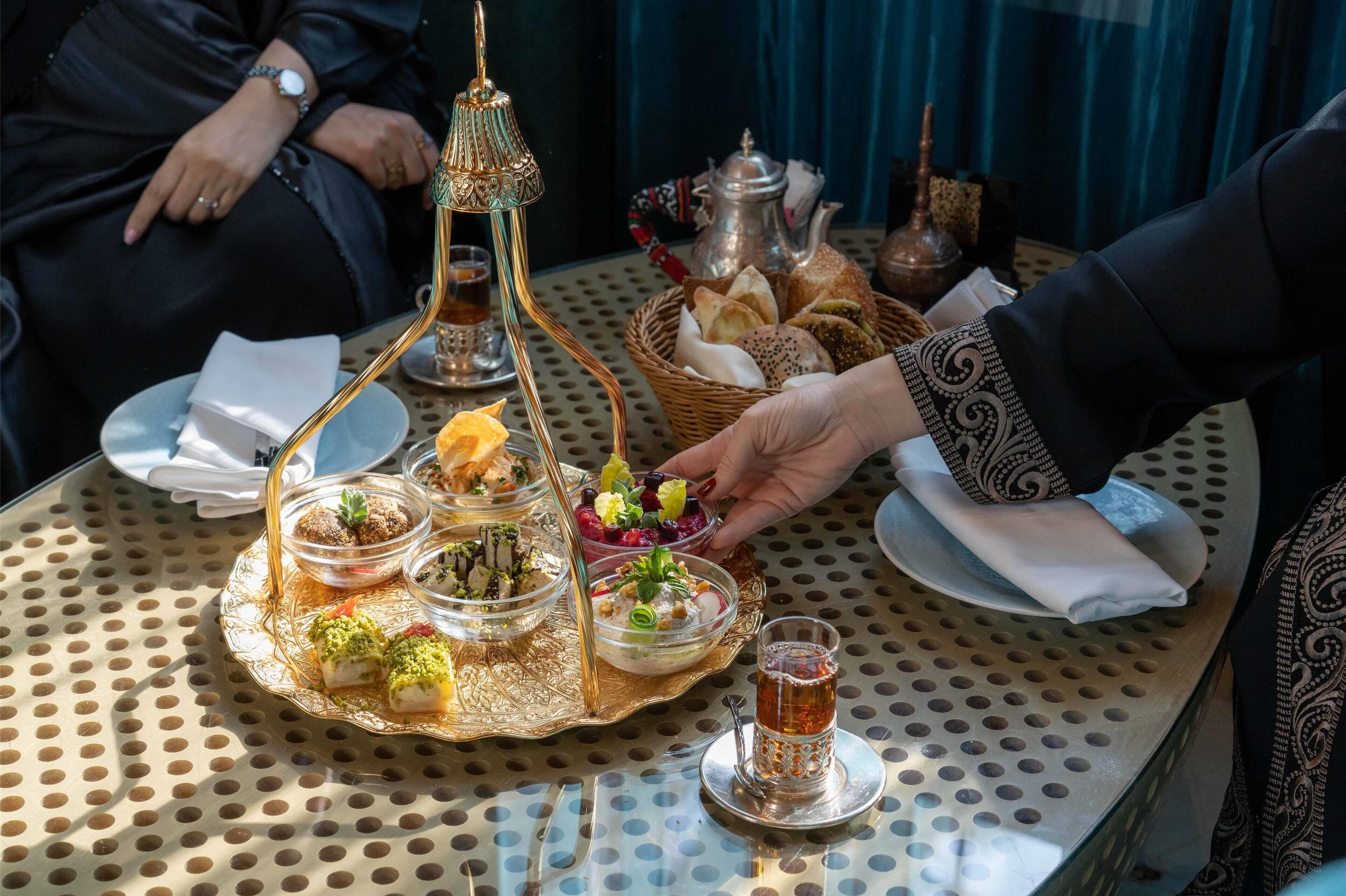 A table with a variety of dishes, including a tray with pastries and a teapot.