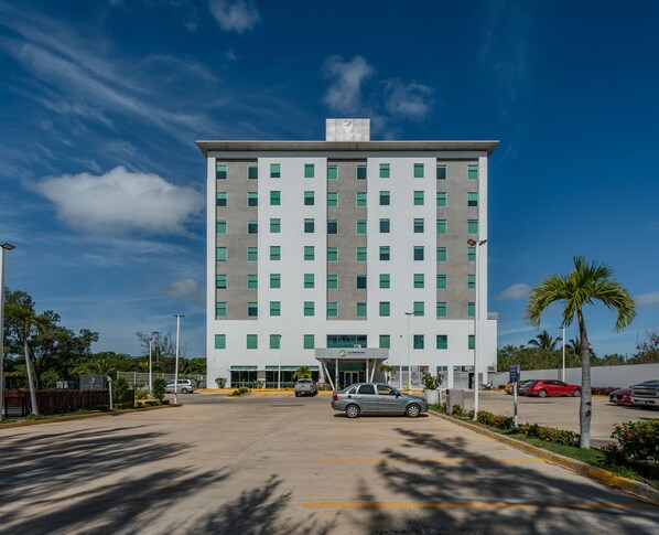 Un hotel de varios pisos con un diseño moderno, que cuenta con una entrada central y un estacionamiento frente a él.