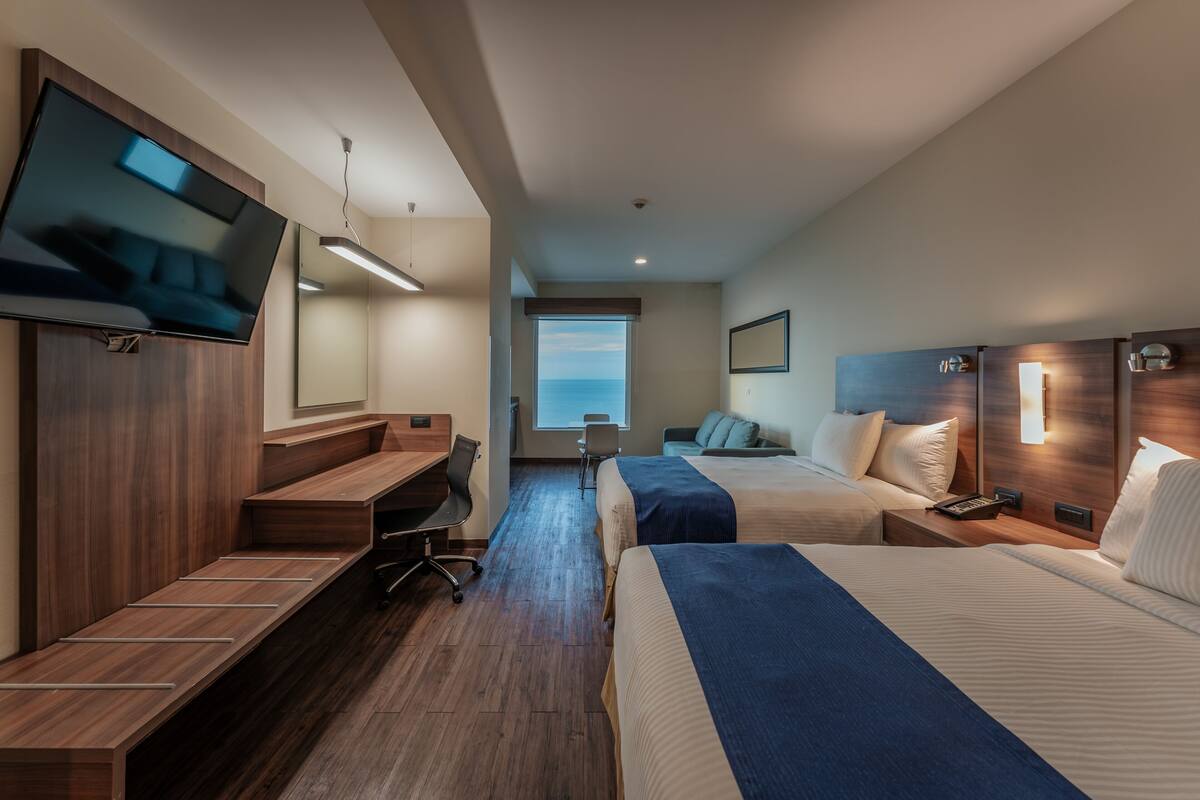A hotel room with a TV, a desk, two beds, a chair, and a window with a view.