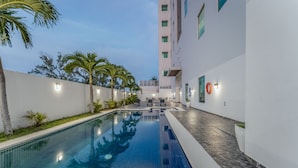 Una piscina con suelo de baldosas, rodeada de paredes blancas y palmeras.