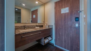 A modern bathroom with a granite countertop, wooden vanity, a mirror, and a wooden door.