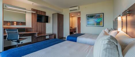 A hotel room with two beds, a desk, a chair, a TV, and an air conditioning unit.
