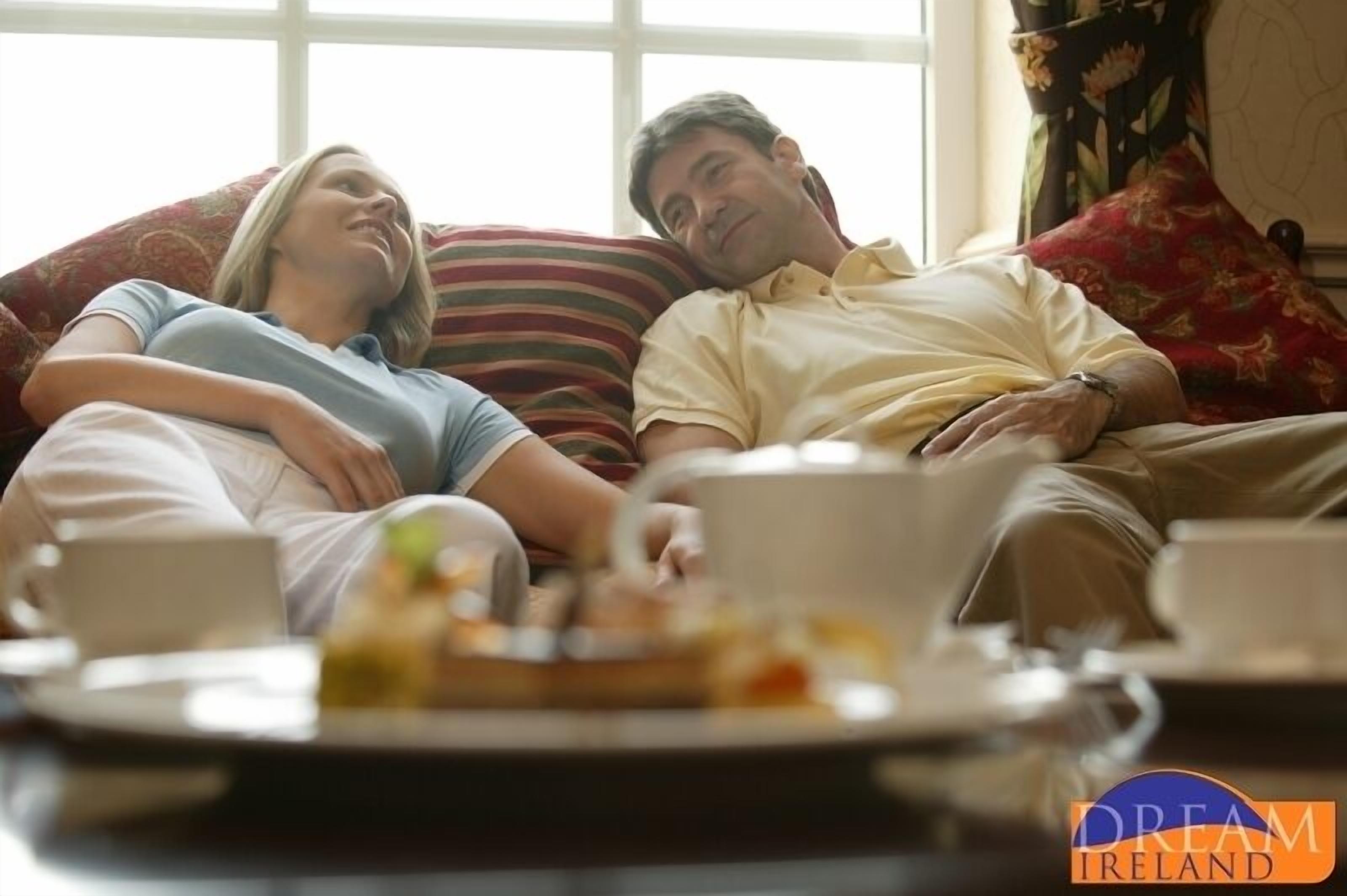 A couple on a bed with a tray of food and cups, suggesting a breakfast setting.