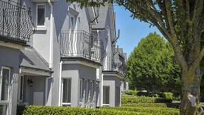 A row of grey townhouses with balconies, neatly trimmed hedges, and a large tree in the foreground. - Wolseley Holiday Lodges (Tullow)