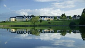 A large, multi-story building with a symmetrical facade, situated next to a calm body of water reflecting its structure. - Wolseley Holiday Lodges (Tullow)