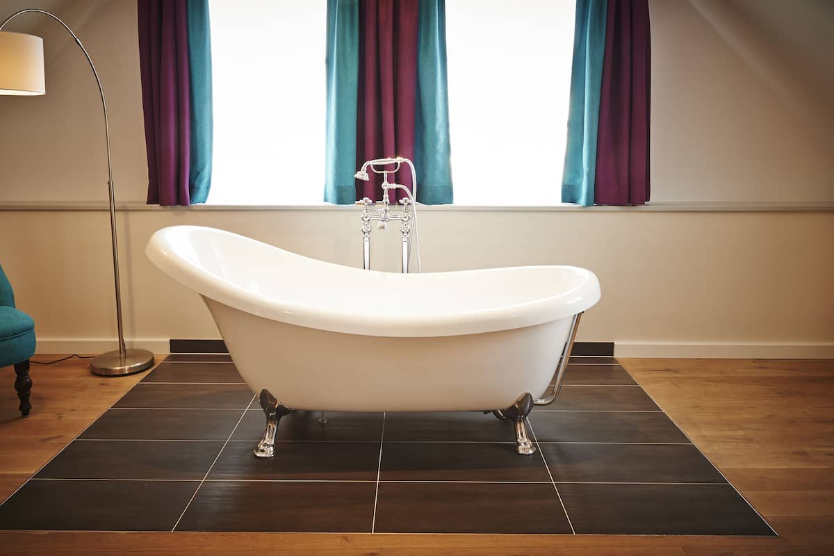 A modern bathroom with a freestanding bathtub, a floor lamp, and a teal sofa.