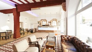 Un vestíbulo con piso a cuadros, asientos de cuero, vigas de madera y una recepción con ventanas arqueadas.