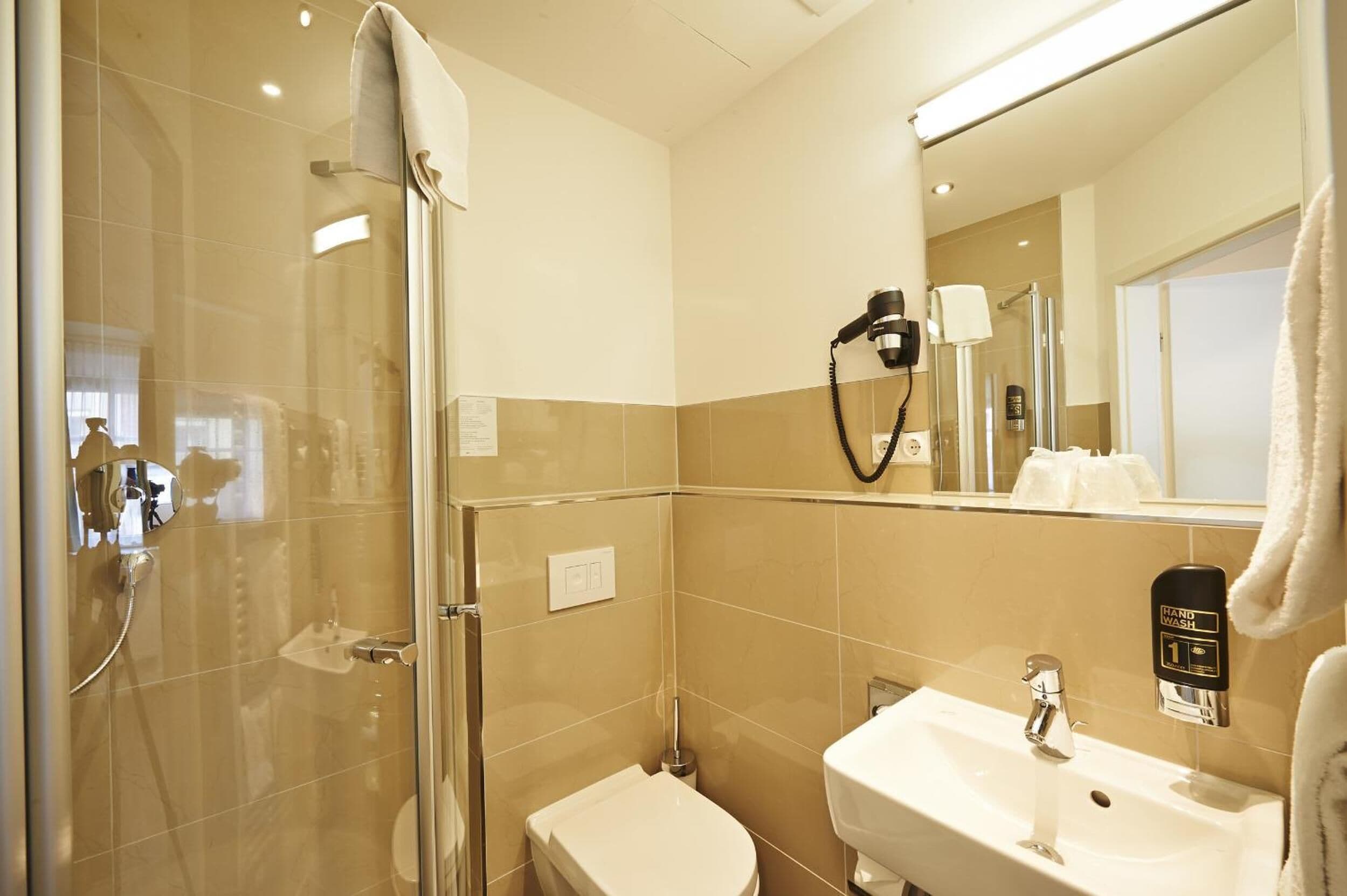 A modern bathroom with a glass-enclosed shower, a white sink, and a handheld hair dryer mounted on the wall.