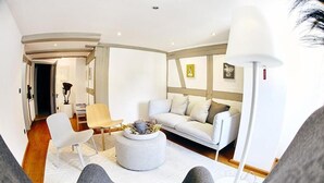 Una sala de estar moderna con un sofá, un reposapiés y sillones, una lámpara, y un pasillo que conduce a otra habitación.