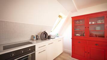 A kitchen with white cabinetry, a red cabinet with glass doors, and a window above the sink.