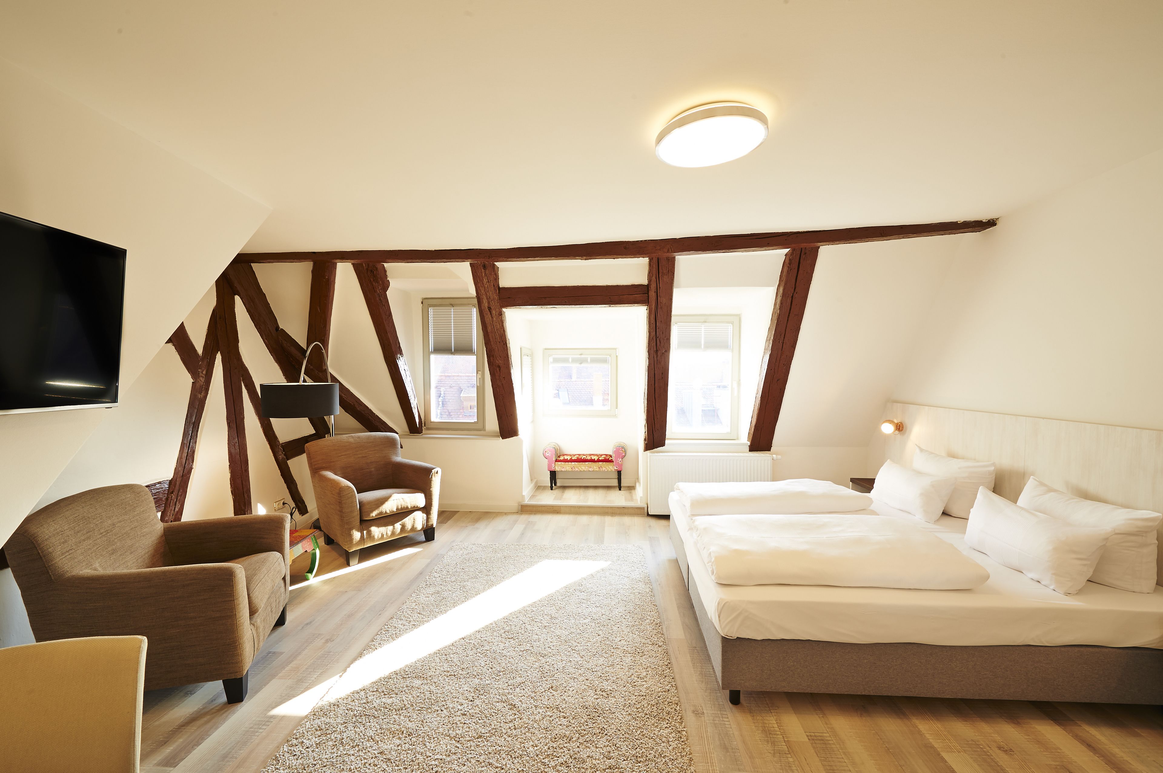 A bedroom with a bed, a sofa, a TV, and a window.