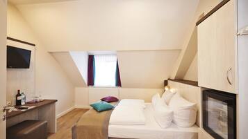 A compact hotel room with a bed, a small desk, a television, and a window with curtains.