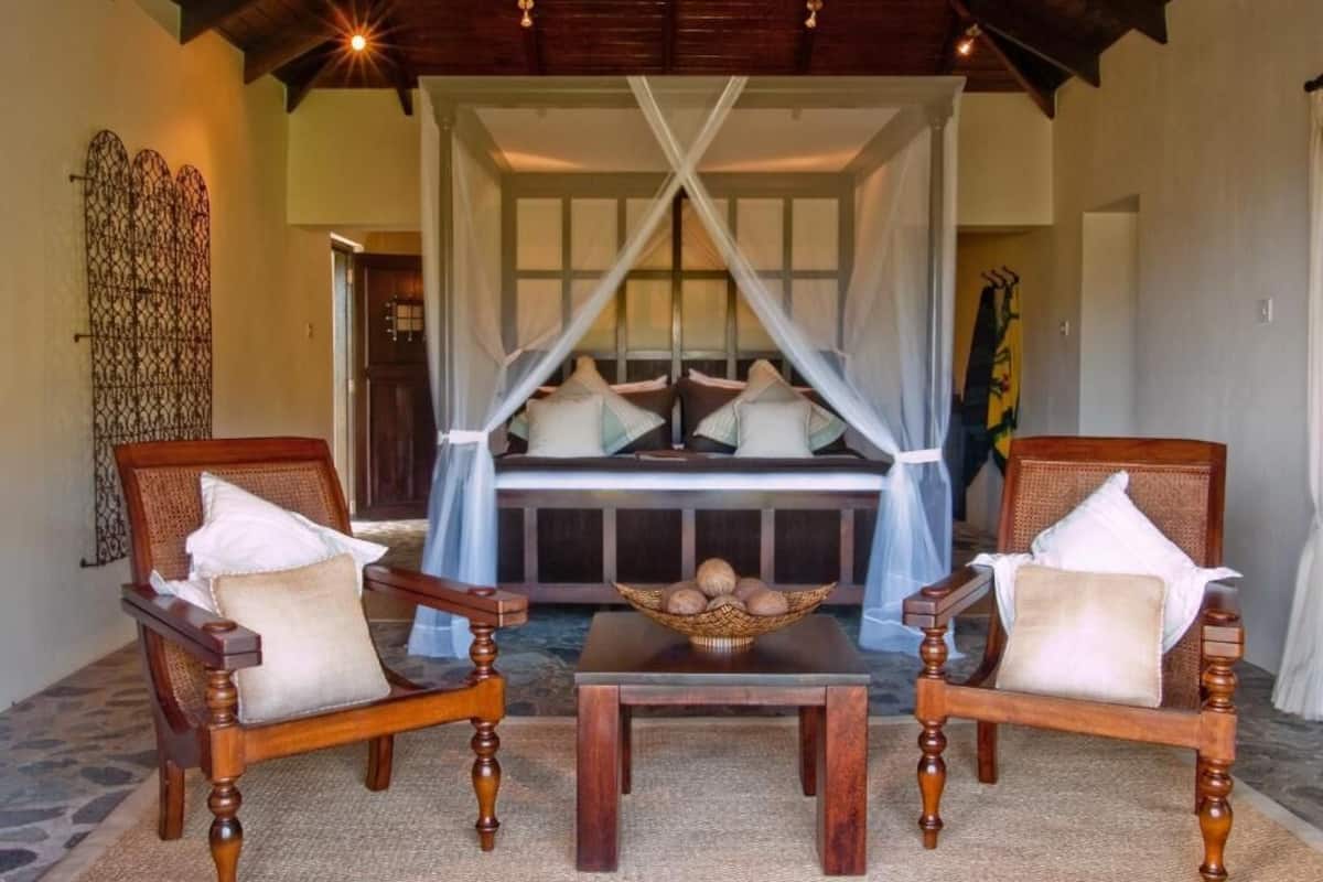 A room with a canopy bed, two wooden chairs, a table, and a decorative basket.