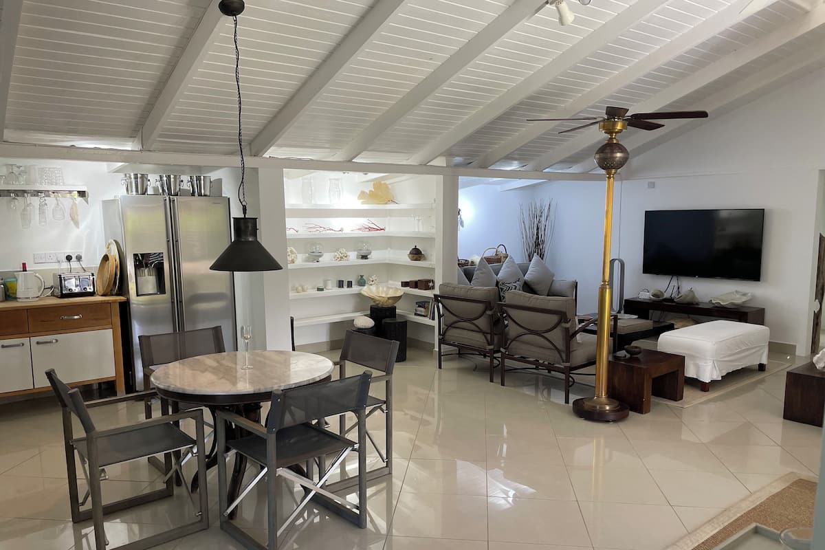A modern kitchen with a dining area, a living room with a TV, and a ceiling fan.