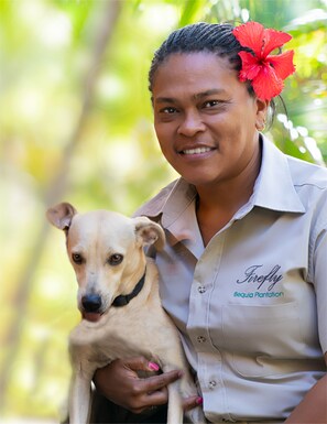 A person holding a dog, wearing a shirt with "Firefly Bequia Plantation" text, outdoors with greenery in the background. - Firefly Estate Bequia (Bequia Island)