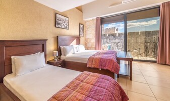 Habitación de hotel con dos camas, una mesita y un balcón con vistas a un edificio histórico.