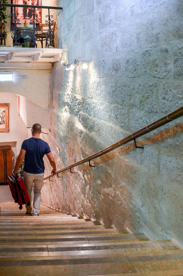 A man descending a stone staircase with a railing, surrounded by a textured wall and a wooden door. - New Imperial Hotel (Jerusalem)