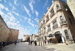 Una calle adoquinada flanqueada por edificios históricos, un muro de piedra y un cielo azul despejado.