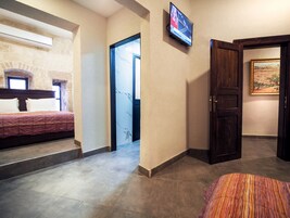 Habitación de hotel con una cama, televisor montado en la pared, una puerta y un cuadro.