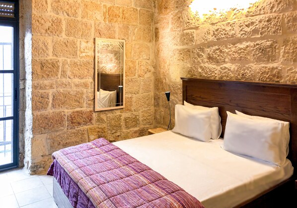 A bedroom with a stone wall, a wooden headboard, and a bed with white and purple bedding.