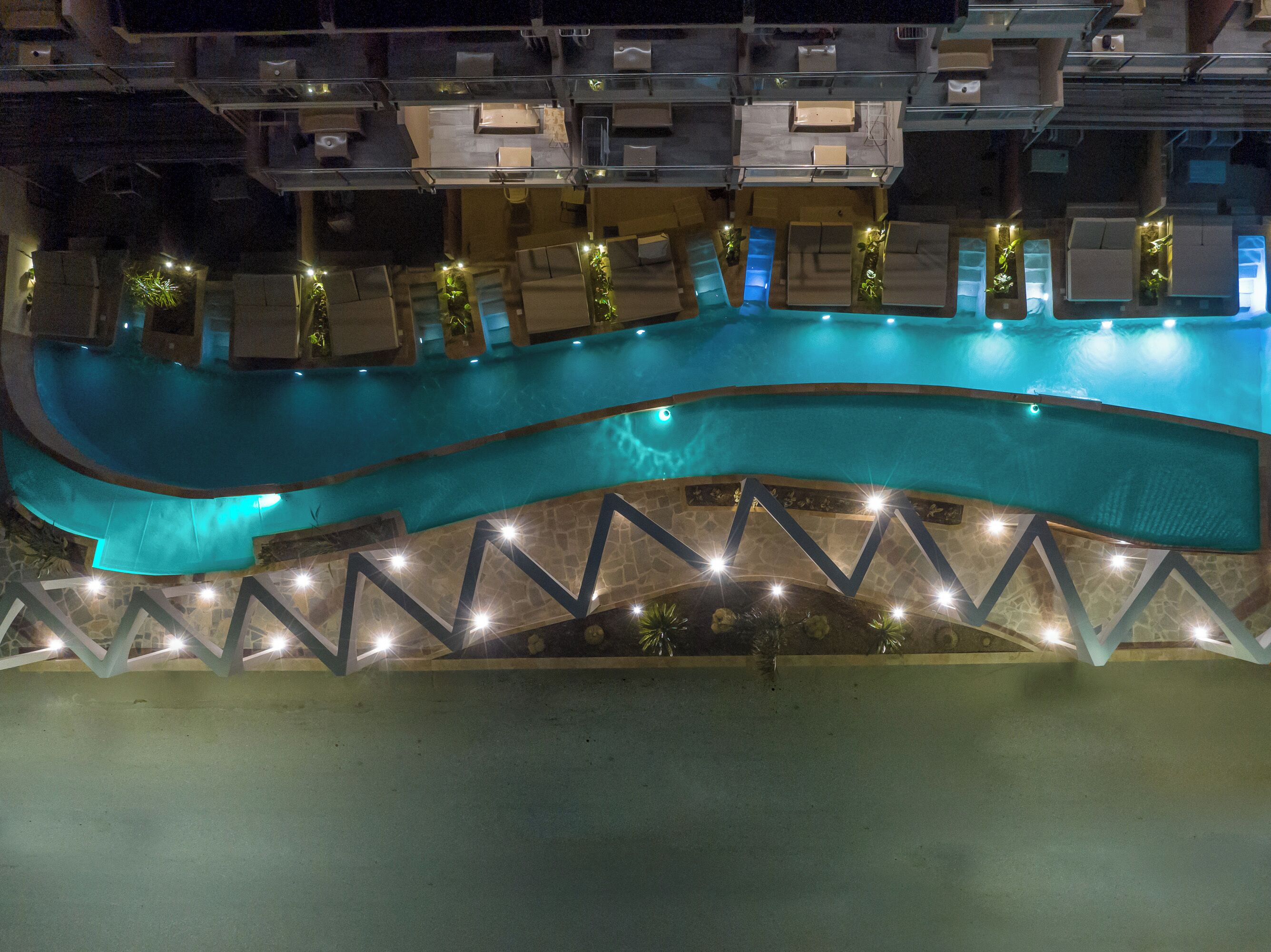 A swimming pool with a curved design, surrounded by a stone deck and illuminated by lights.