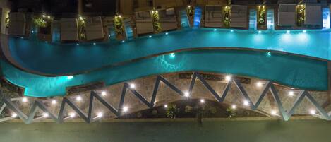 A swimming pool with a curved design, surrounded by a stone deck and illuminated by lights.
