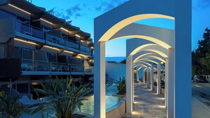 A modern hotel with a pool area, outdoor seating, and a view of the sea.