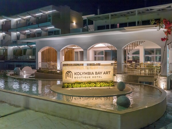 A hotel entrance with a sign for 'Kolymbia Bay Art Boutique Hotel' and a pool area.