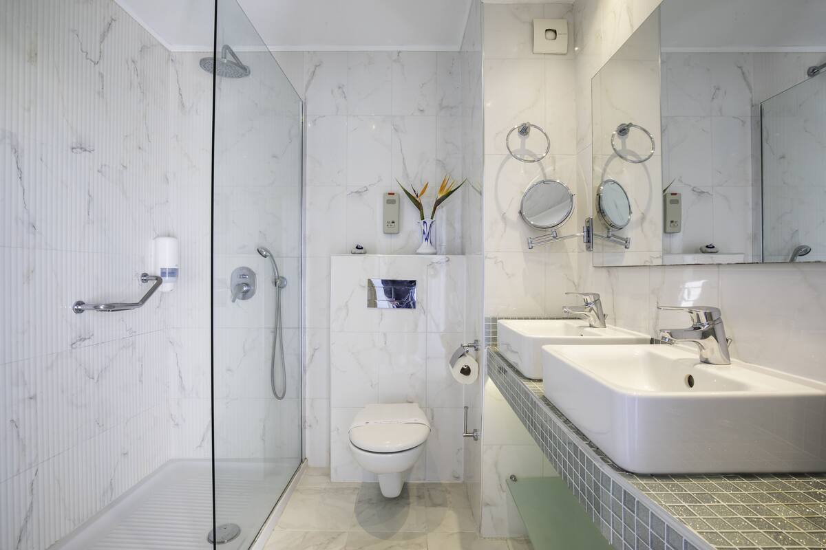 Een moderne badkamer met een glazen douchecabine, toilet en een dubbele wastafel met spiegel erboven.