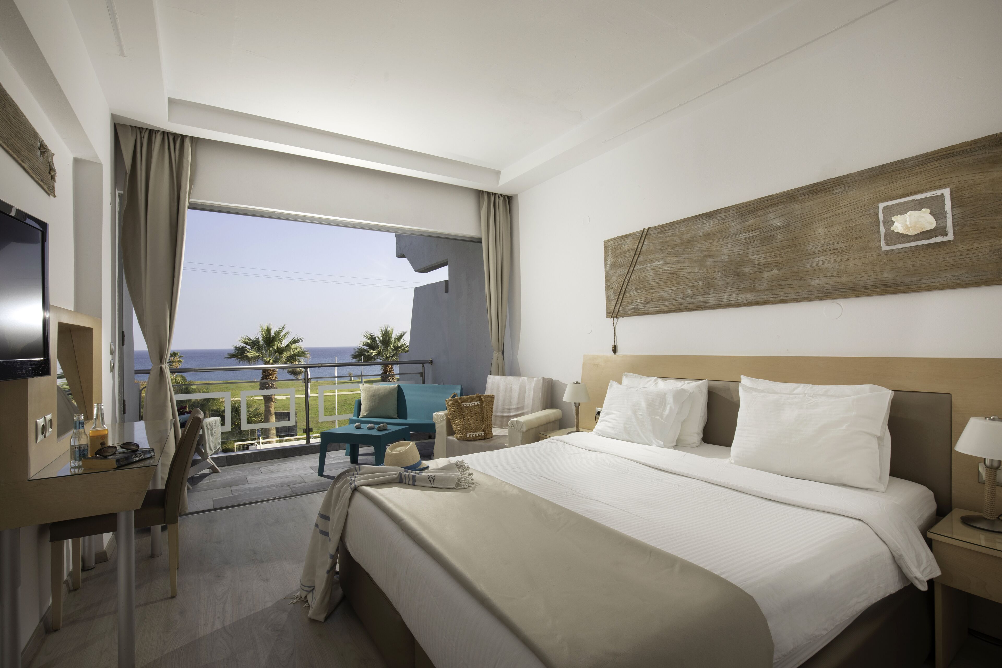 Een hotelkamer met een groot bed, een bureau, een stoel, een televisie en een balkon met uitzicht op zee.