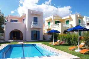 A swimming pool with a tiled edge, a covered patio area, and a building with balconies and outdoor seating.