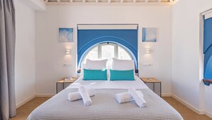 A bedroom with a large bed, two bedside tables, a window with a view, and a ceiling with exposed beams.