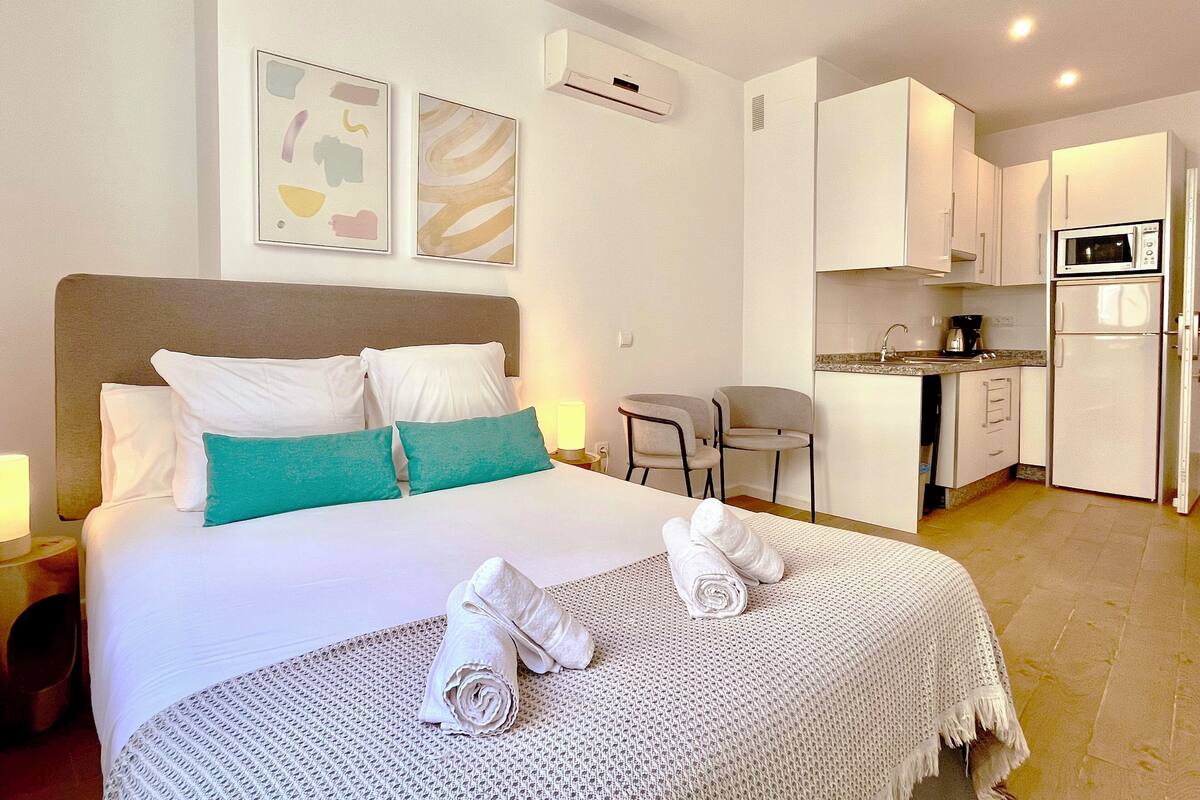 Habitación de hotel con cama, una kitchenette pequeña y dos cuadros en la pared.