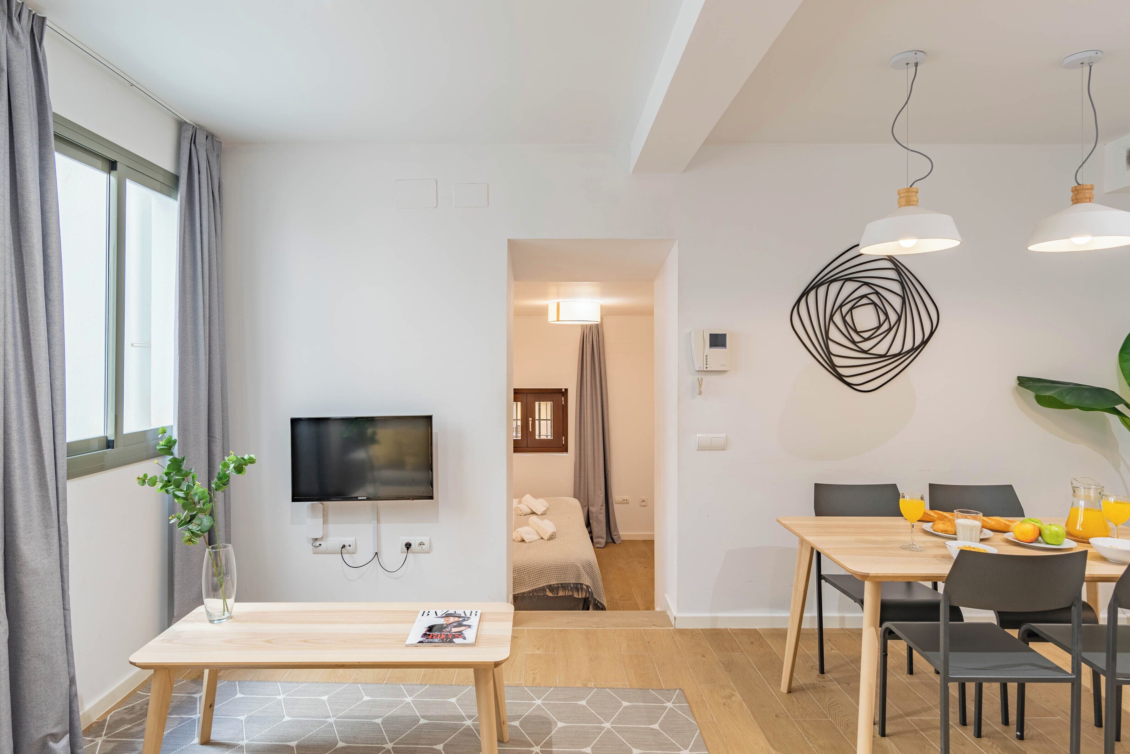 A modern hotel room with a dining area, a TV, and a bed.
