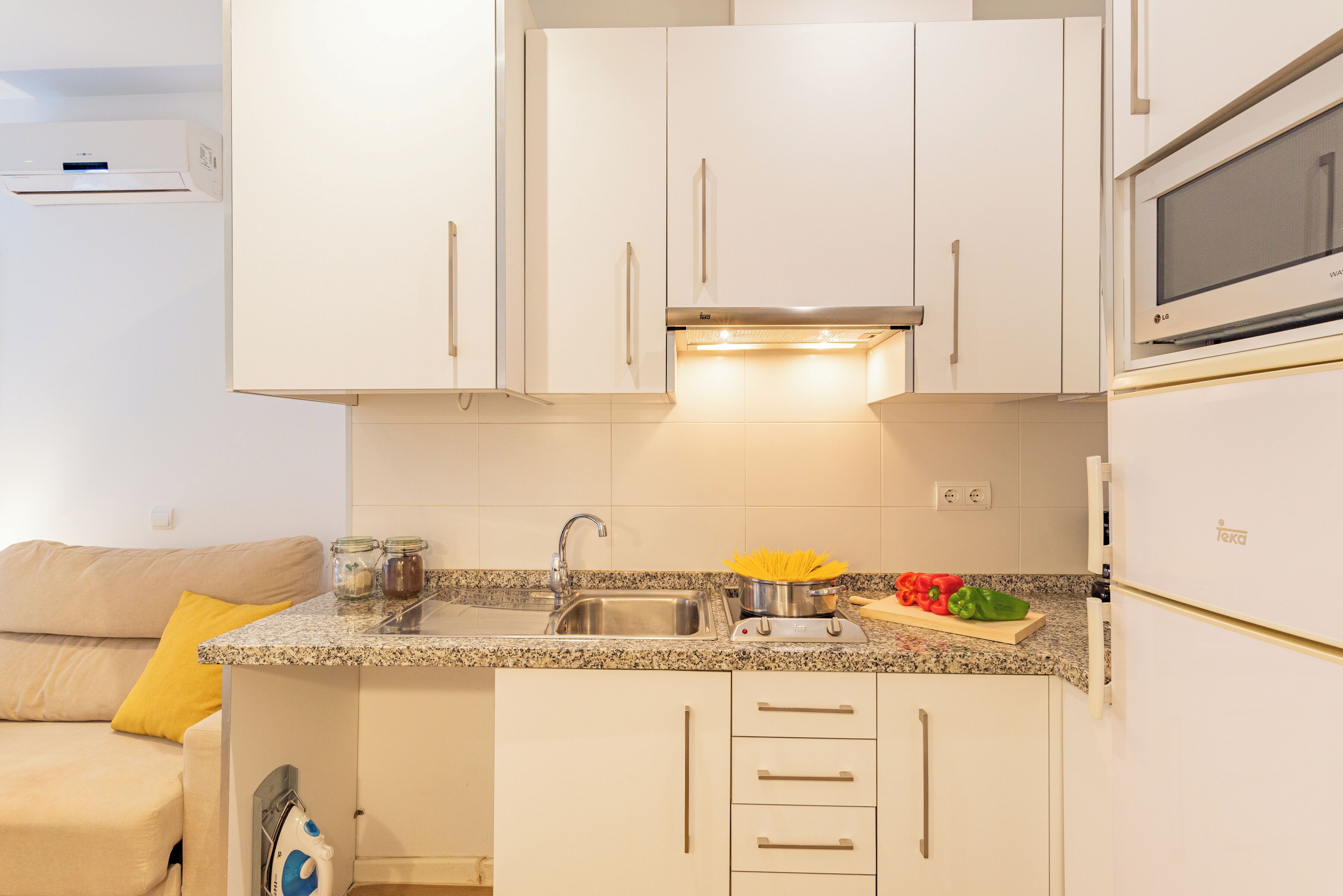 A compact kitchen with white cabinets, a stainless steel sink, and a microwave.