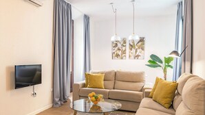 A modern living room with a sofa, a glass coffee table, a flat-screen TV, and a plant.