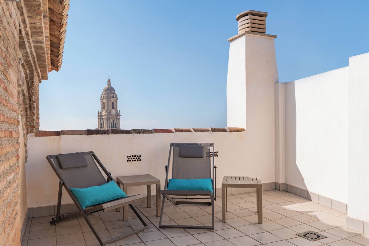 Terraza en la azotea con dos sillones de descanso, una mesita y vista a un edificio histórico.
