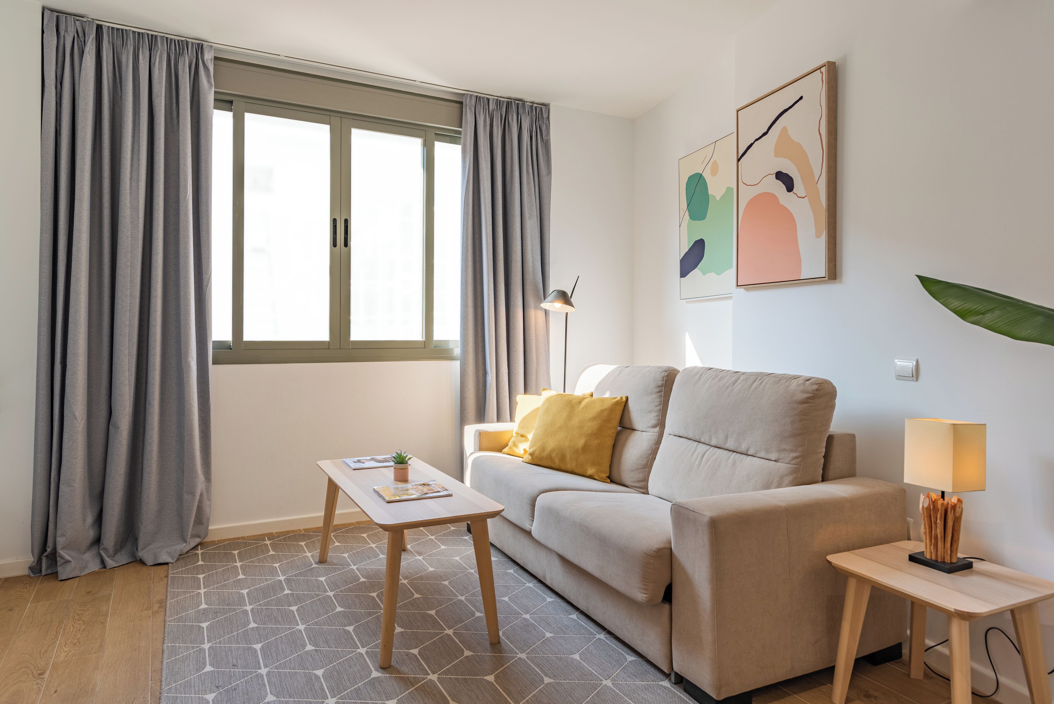 A living room with a sofa, a coffee table, a lamp, and a window with curtains.