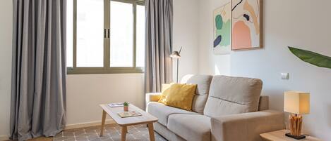 A living room with a sofa, a coffee table, a lamp, and a window with curtains.