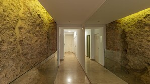 A hallway with stone walls and a glass partition, leading to a door at the end.
