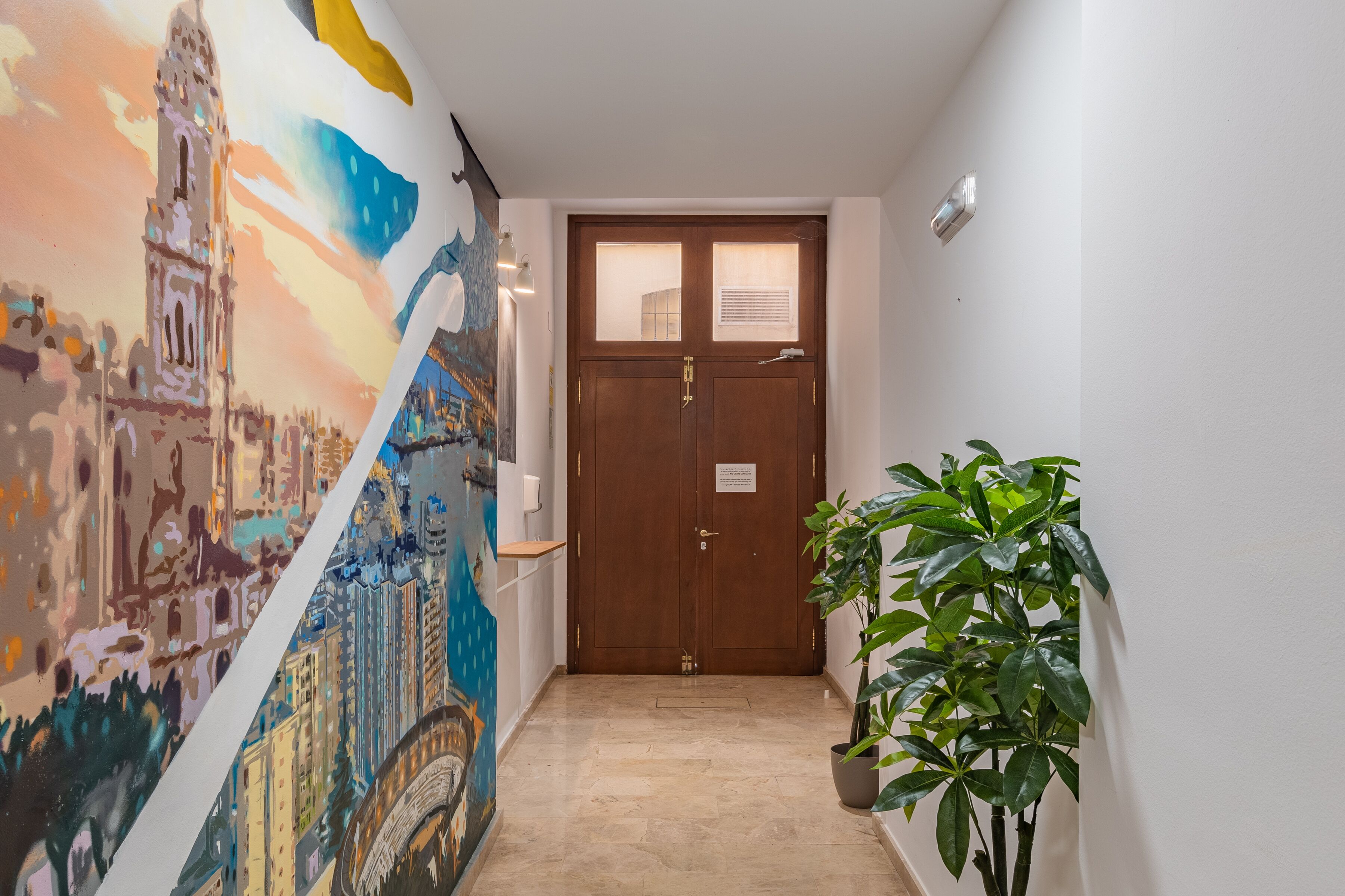 A hallway with a wooden door, a wall mural, and a potted plant.