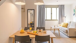 A modern dining area with a wooden table, black chairs, and a breakfast setup including a croissant, fruits, and orange juice.